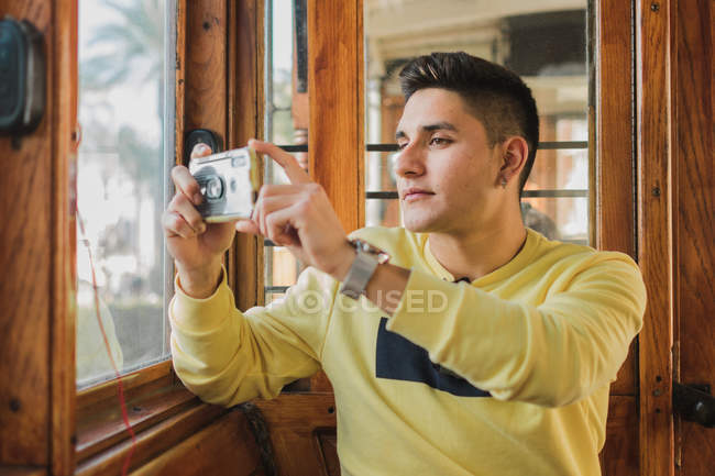 Стильний молодий чоловік мандрівник у повсякденному одязі фотографується на мобільному телефоні під час їзди в старому поїзді — стокове фото