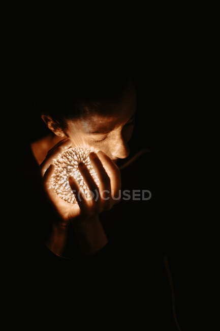 Alto ângulo de mulher nua cobrindo peito com mão e segurando bola luminosa no escuro — Fotografia de Stock
