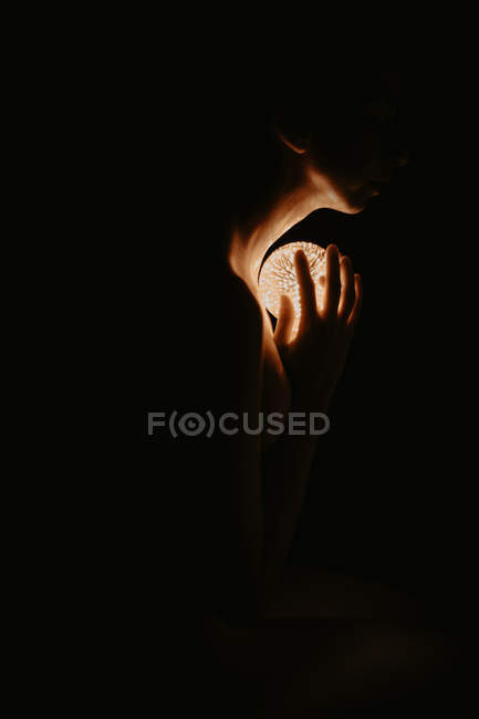 High angle of naked woman covering chest with hand and holding luminous ball in dark — Stock Photo