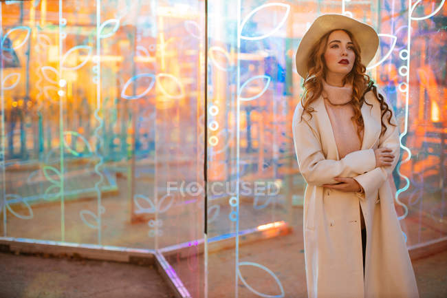 Mulher bonita na moda casaco branco de pé à luz dos sinais de néon na rua da cidade — Fotografia de Stock
