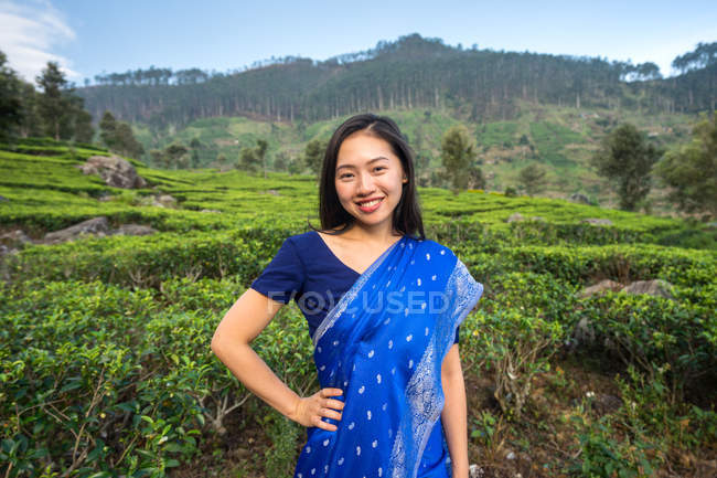 Весела жінка в синьому традиційному одязі, яка дивиться на камеру, стоячи на чайних луках у Хапуталі (Шрі - Ланка). — стокове фото