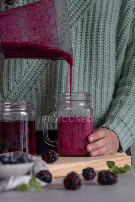 Crop person filling from blender glass jar with yummy vitamin smoothie of sweet fresh berries and mint after preparing breakfast at home — Stock Photo