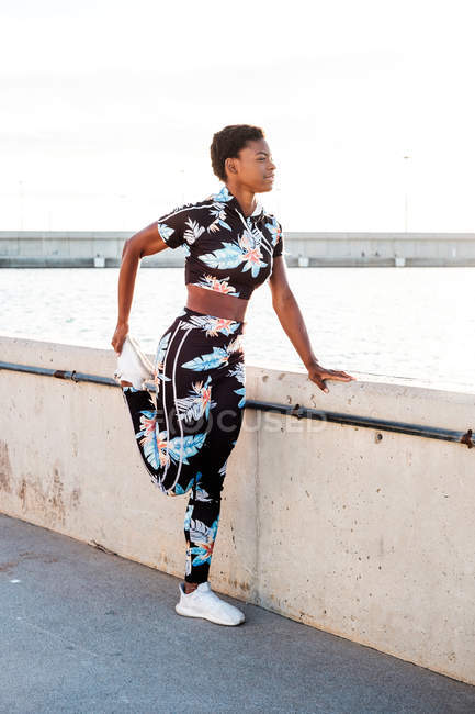 Mujer adulta afroamericana en ropa deportiva flores estira los músculos de las piernas mientras