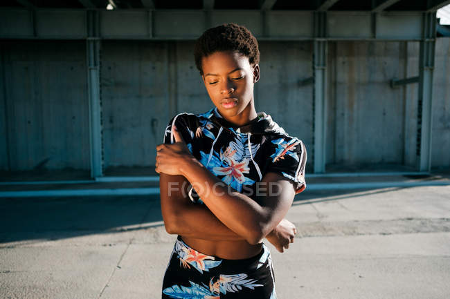 African American female athlete in flowered sportswear with closed eyes while standing alone on street in sunbeams against concrete wall in city — Stock Photo