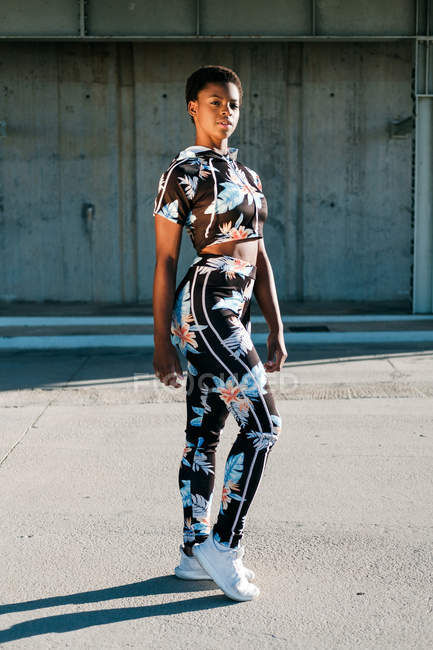 Афроамериканська спортсменка у квітучій спортивній манері дивиться на камеру з викликом, стоячи на вулиці в сонячних променях проти бетонної стіни міста. — стокове фото