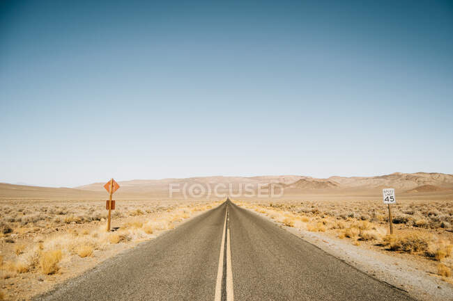 Estrada reta vazia com sinais de trânsito no deserto dos EUA no dia ensolarado — Fotografia de Stock