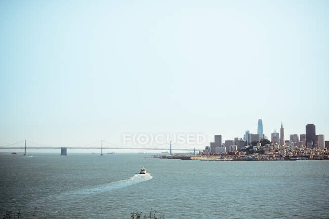 Човен пливе на річці поблизу сучасного міста США проти ясного блакитного неба в сонячний день. — стокове фото