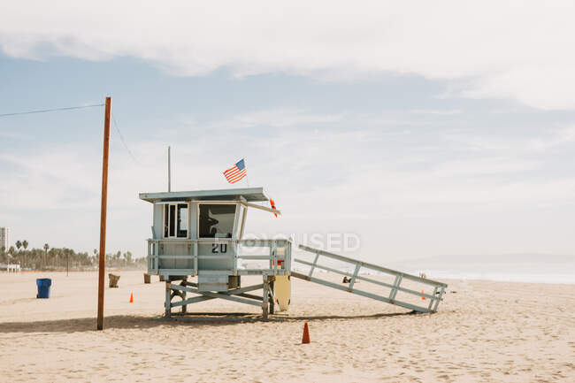 Suporte salva-vidas de madeira com bandeira dos EUA na praia de areia na Califórnia no dia ensolarado — Fotografia de Stock