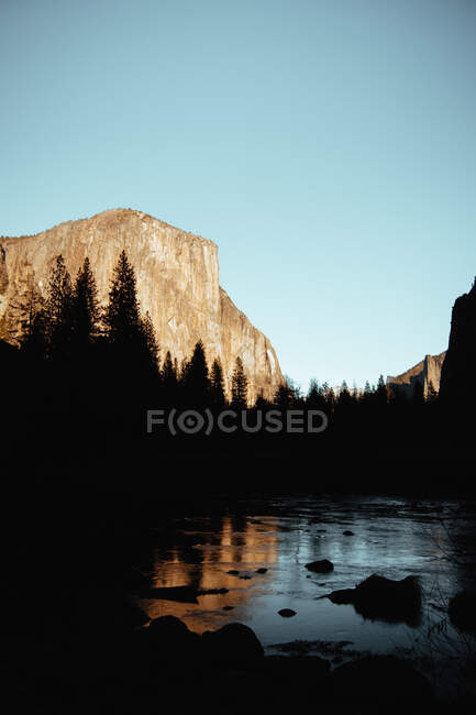 Dark silhouette of high forest trees around lake reflecting sky and mountain in USA — Stock Photo