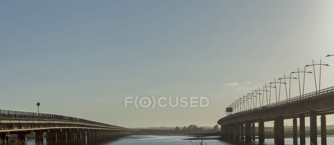 Wide angle of modern bridges crossing river against cloudless sundown sky in countryside — Stock Photo