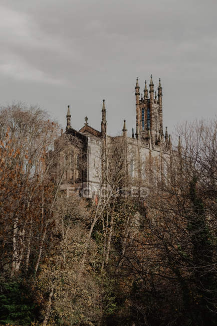 Shabby facade of ancient house with towers and exhaust pipes against cloudy sky in bushes of town — Stock Photo
