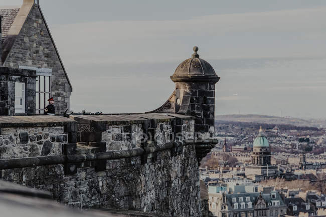 Male guard in uniform standing on roof of historic stone building against gray sky in city in Edinburgh, Scotland, UK — Stock Photo