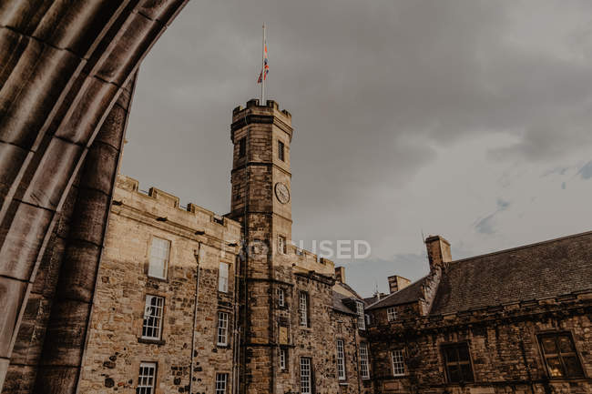 Dal basso antico edificio in pietra con bandiera sulla torre dell'orologio situato contro cielo grigio nuvoloso — Foto stock