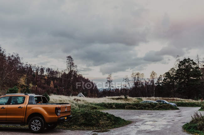 Auto arancione su strada in campagna vicino foresta autunnale dopo la pioggia il giorno nuvoloso — Foto stock