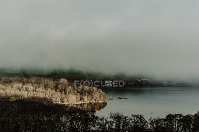 Dall'alto di nebbia foresta autunnale con raggi di luce solare vicino lago con nebbia — Foto stock