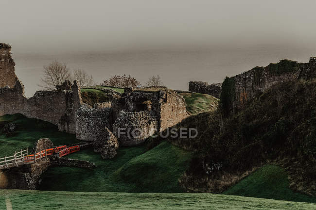 Разрушенный старый каменный замок с мостом и зеленой лужайкой в облачный день — стоковое фото