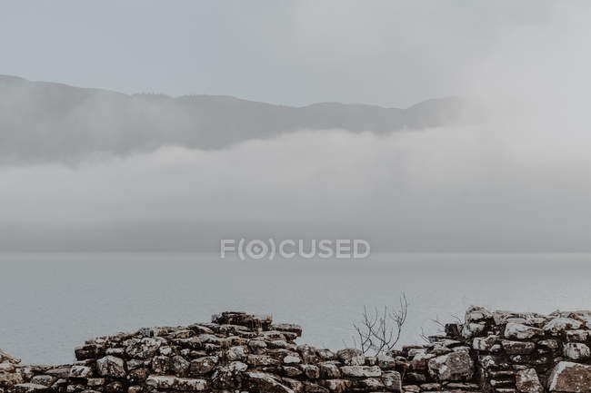 Parede de pedra do antigo castelo arruinado contra o céu nublado com vista para montanhas nebulosas — Fotografia de Stock