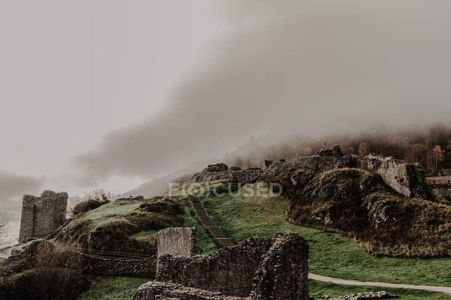 Distrutto vecchio castello di pietra con nebbia con pareti e scale con torre su nuvoloso giorno — Foto stock