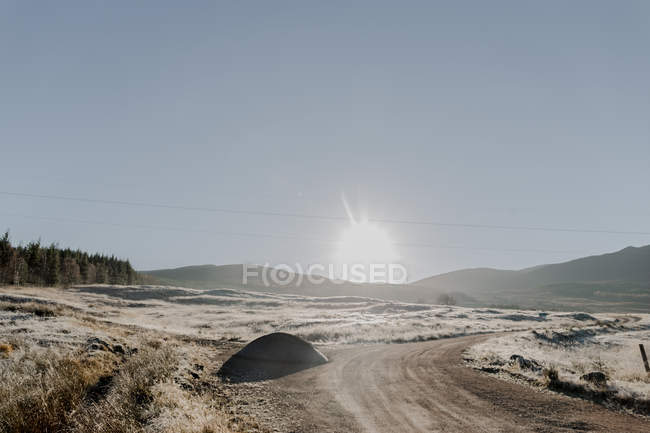 Заснеженная дорога с поворотом в сельской местности, проходящей через горы на восходе солнца — стоковое фото