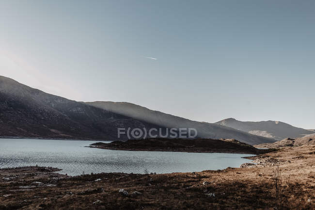 Scenic landscape of mountains with rocks and lake against clear blue sky at sunrise — Stock Photo