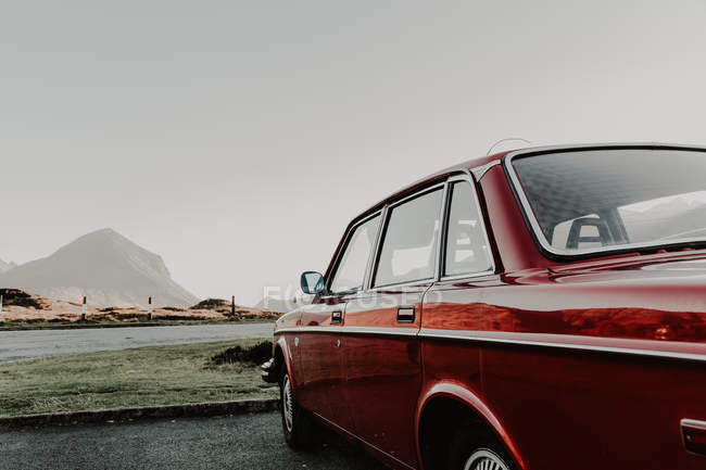 Side view of antique red automobile on road passing through mountains on cloudy daytime — Stock Photo