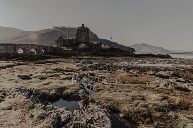 Castelo de pedra com arquitetura envelhecida com ponte perto do rio no dia ensolarado — Fotografia de Stock