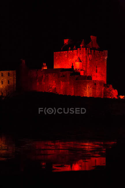 Paesaggio notturno di antico maestoso castello sulla riva del fiume illuminato da luce rossa al buio — Foto stock