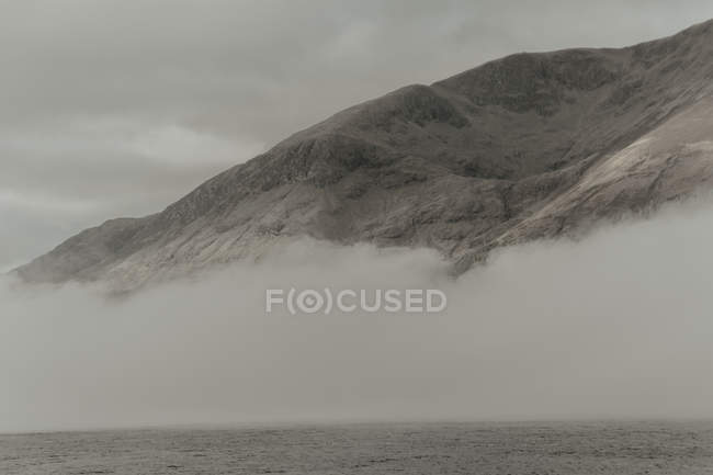 Одинокие вершины окружены облаками под серым небом в туманное время дня — стоковое фото