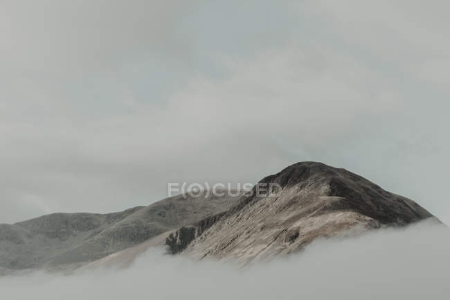 Sommets solitaires entourés de nuages sous un ciel gris dans le brouillard diurne — Photo de stock