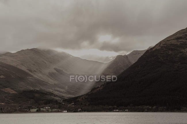 Ruhiger Fluss umgeben von steinigen Bergen unter Sonnenlicht und grauem Himmel — Stockfoto