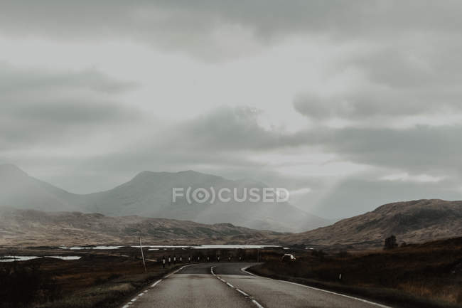 Асфальт обозначен проездом между коричневыми сухими холмами долины под серым небом — стоковое фото