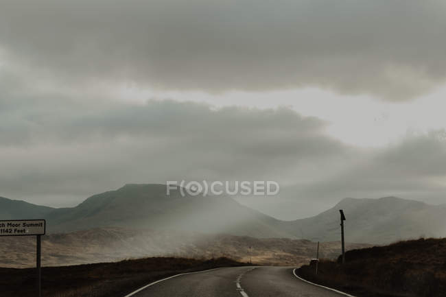 Route balisée en asphalte entre collines brunes et sèches de la vallée sous un ciel gris — Photo de stock