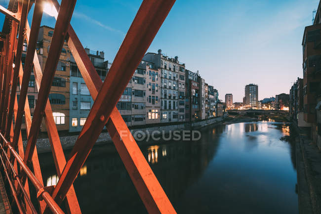 Paisagem pitoresca da cidade de edifícios de apartamentos localizados no canal atrás de trilhos de ponte vermelha no início da noite, Girona, Espanha — Fotografia de Stock