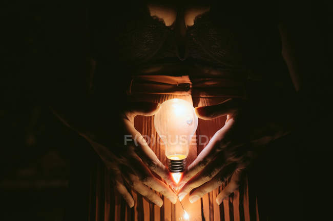 Середина женщины, держащей в руках лампочку в темноте — стоковое фото