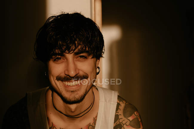 Young stylish guy with mustache and tattoos in white tank top, looking in camera — Stock Photo