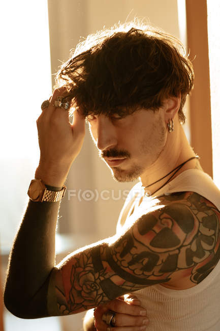 Seitenansicht eines stylischen Typen mit Tattoos, der sich an die Wand lehnt und in die Kamera schaut — Stockfoto