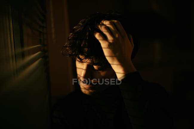 Красивий меланхолійний хлопець у чорному черепашці, що стоїть поруч з вікном з жалюзі — стокове фото