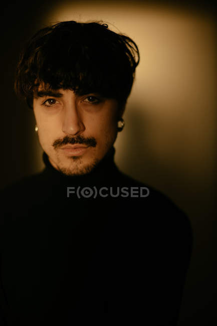 Jeune homme avec moustache à côté du mur regardant dans la caméra — Photo de stock