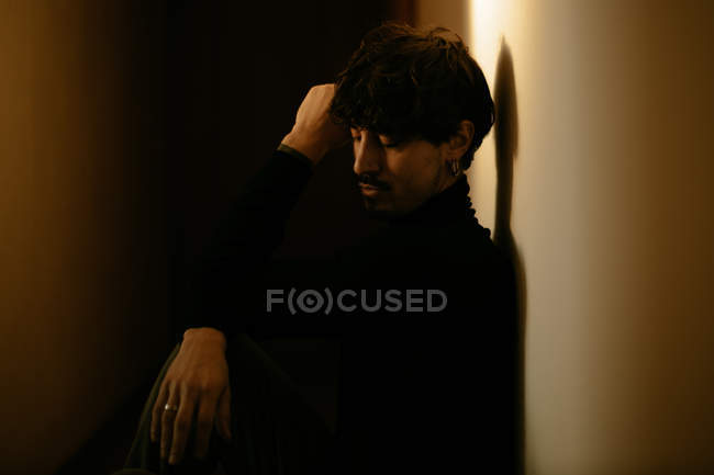 Young man with mustache sitting next to wall and running fingers through hair with closed eyes — Stock Photo