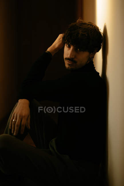 Nachdenklicher Mann mit Schnurrbart sitzt mit erhobenem Arm an Wand — Stockfoto