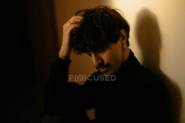 Молодой модный мужчина с усами сидит рядом со стеной с поднятой рукой над головой — стоковое фото