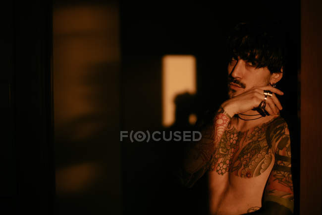 Hombre guapo sin camisa tatuado posando sensualmente a la luz del sol - foto de stock