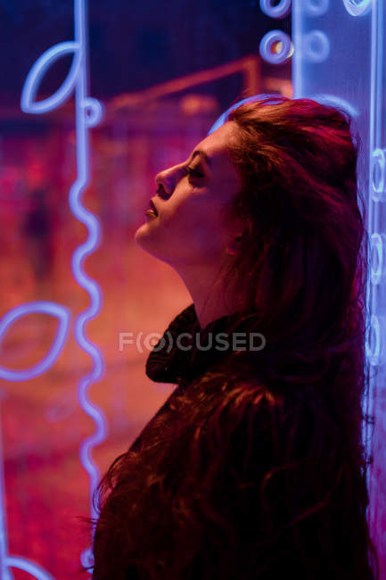 Stilvolle melancholische Brünette im Licht von Leuchtreklamen, die sich an die Wand an der Stadtstraße lehnen — Stockfoto