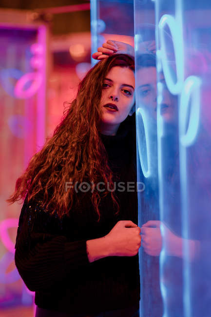 Довольно задумчивая молодая женщина, опирающаяся на стену на городской улице в неоновых вывесках огней — стоковое фото