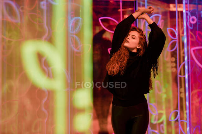 Pretty pensive young woman with closed eyes among neon signs at city street — Stock Photo