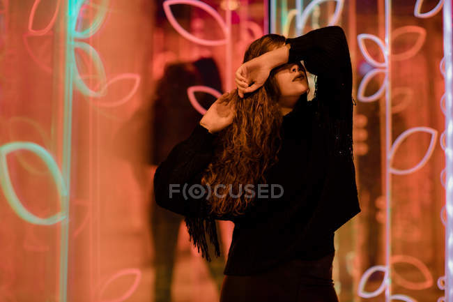 Pretty pensive young woman with closed eyes among neon signs at city street — Stock Photo