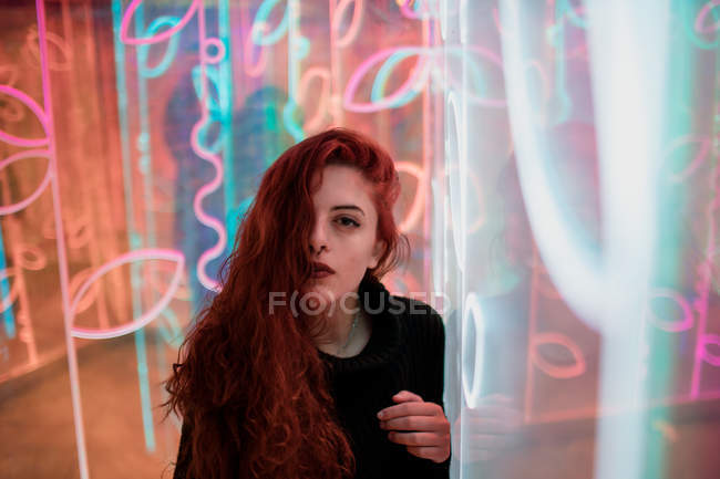 Beautiful melancholic brunette with long hair standing among neon signs at city street — Stock Photo