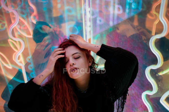 Stylish long-haired woman posing among neon signs at city street — Stock Photo