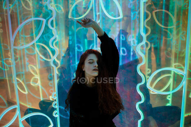 Stylish long-haired brunette in casual wear standing among neon signs at city street — Stock Photo