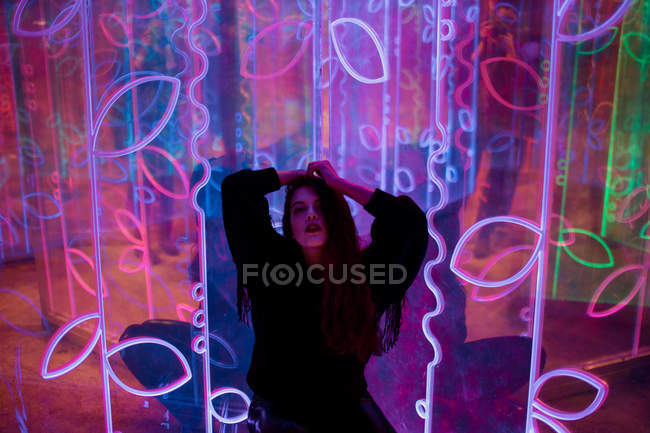 Stylish long-haired brunette in casual wear standing among neon signs at city street — Stock Photo